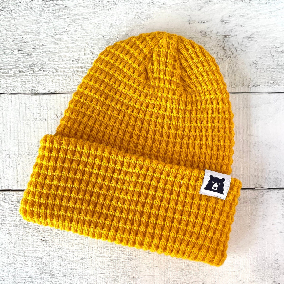 Yellow beanie with a black bear logo on a light wooden surface