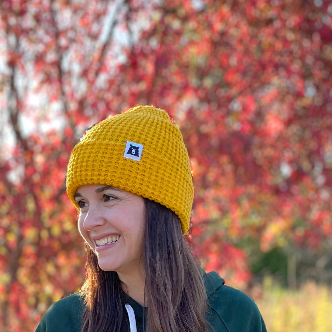 Person wearing a yellow beanie with a logo against a colorful autumn background