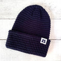 Navy blue knit beanie with a logo tag on a light wooden surface