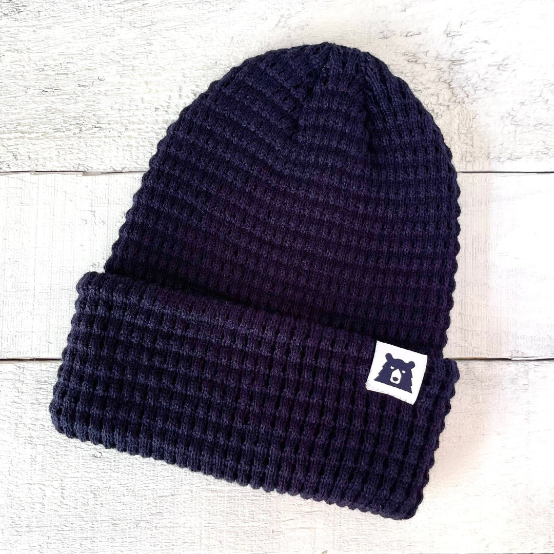 Navy blue knit beanie with a logo tag on a light wooden surface