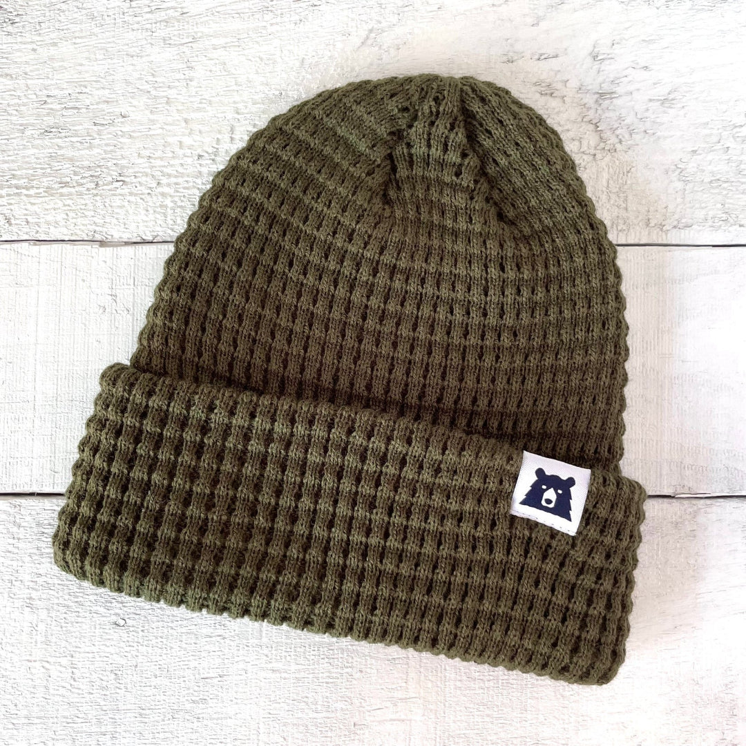 Green knit beanie with a logo on a light wooden background