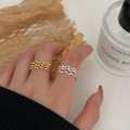 Two wave rings, one in gold plating and one in sterling silver, featuring a modern, abstract, and undulating triple wave design, worn on fingers. These unique rings are available in Ottawa, Ontario, Canada.