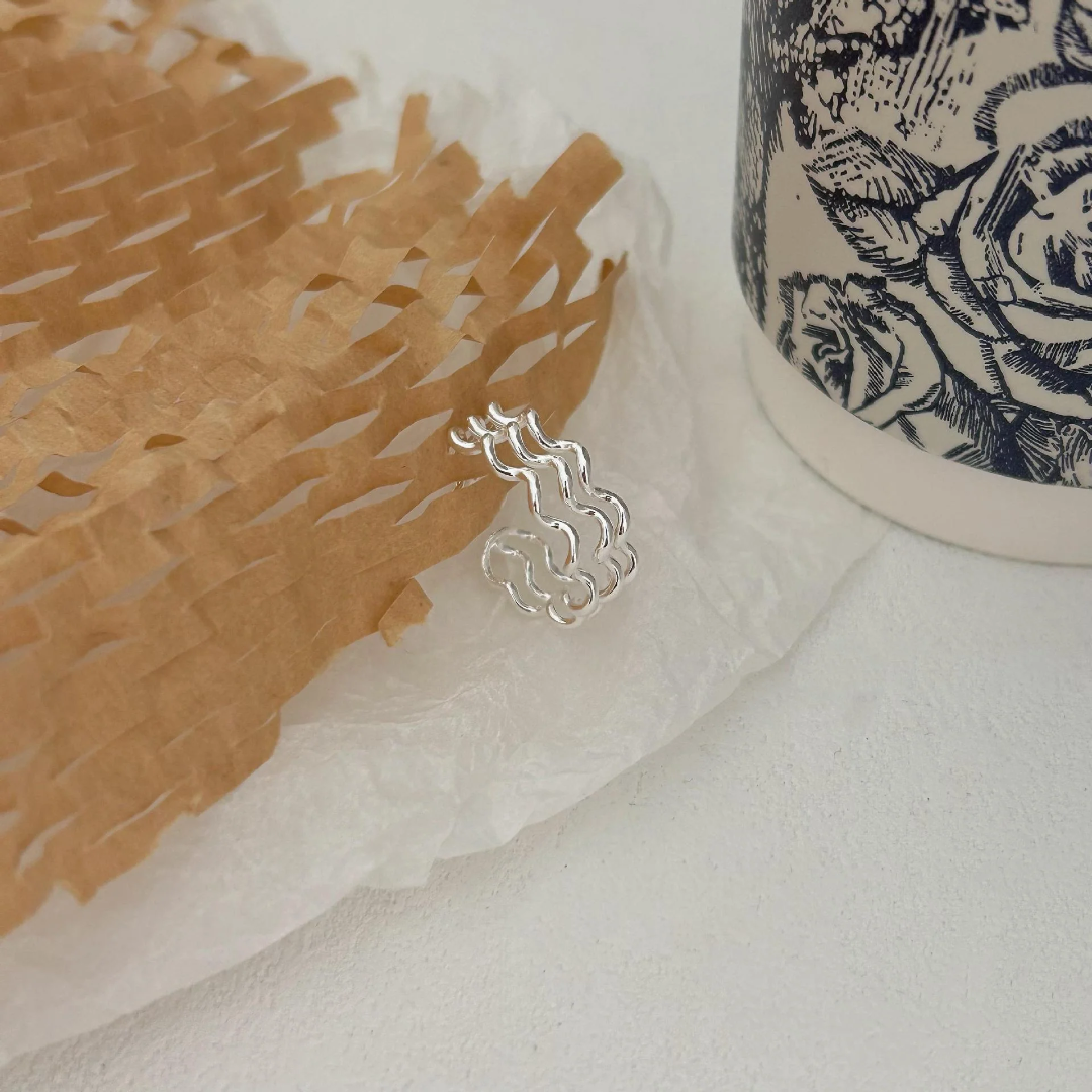 A wave ring made of sterling silver, featuring a modern, abstract, and undulating wavy design, displayed on a light surface with textured paper. This unique ring is available in Ottawa, Ontario, Canada.