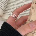 A wave ring made of sterling silver, featuring a modern, abstract, and undulating wavy design, displayed on a light surface with textured paper. This unique ring is available in Ottawa, Ontario, Canada.