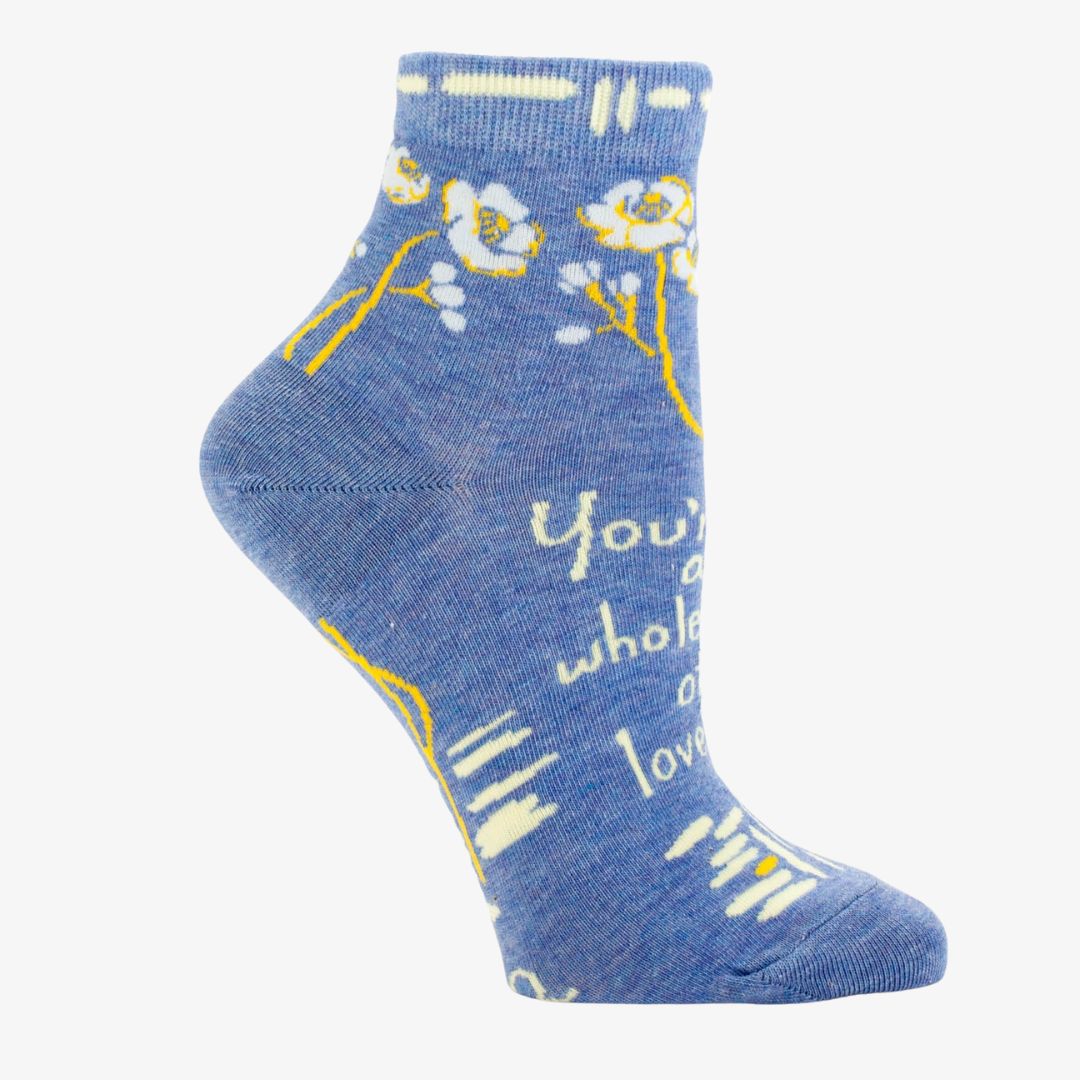 A pair of light blue ankle socks with a pattern of white and yellow flowers and branches. One sock features the text "You're a whole lot of lovely" in white.