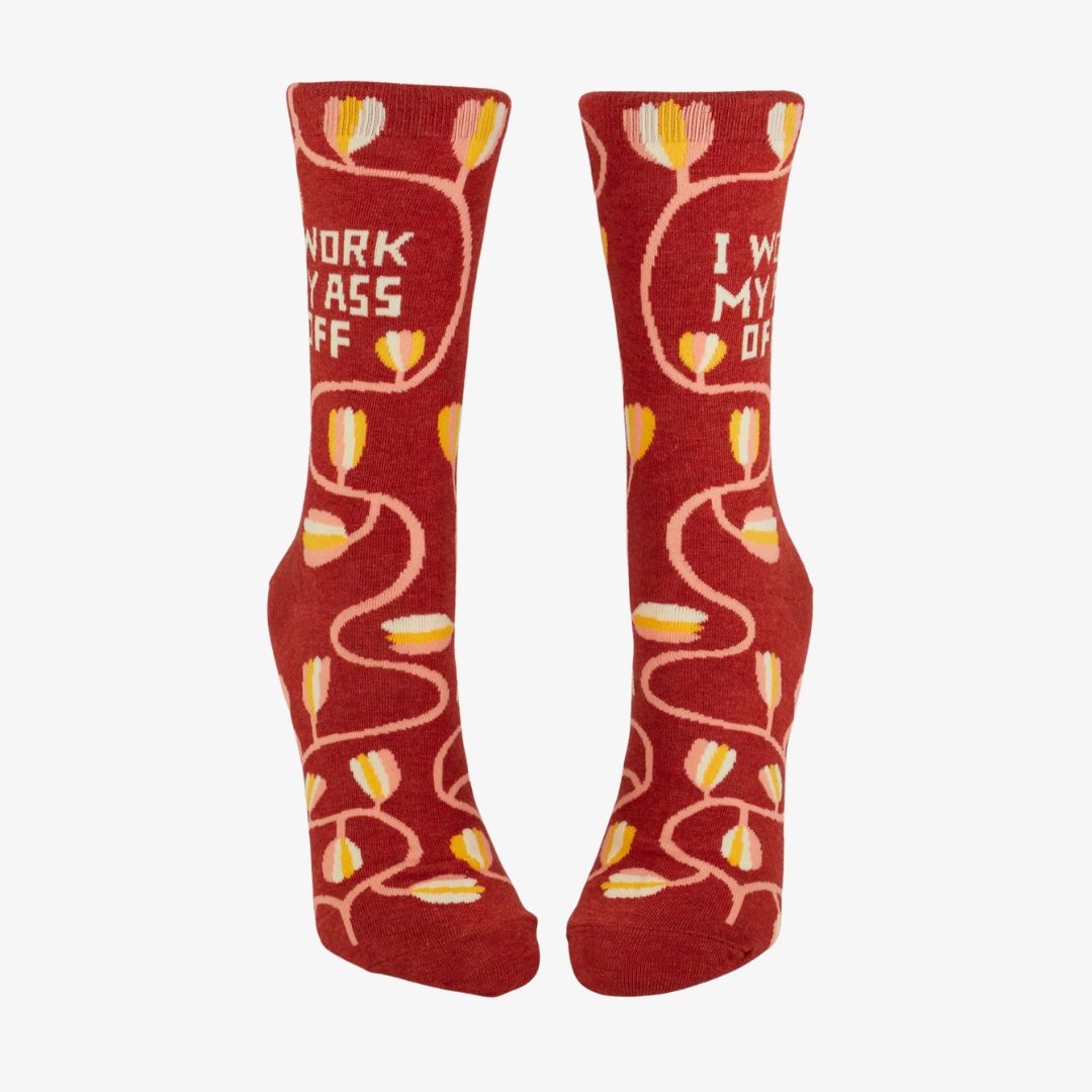 A pair of dark red women's crew socks with a winding vine pattern featuring yellow and pink tulip-shaped flowers. Text on one sock reads "I WORK MY ASS OFF".