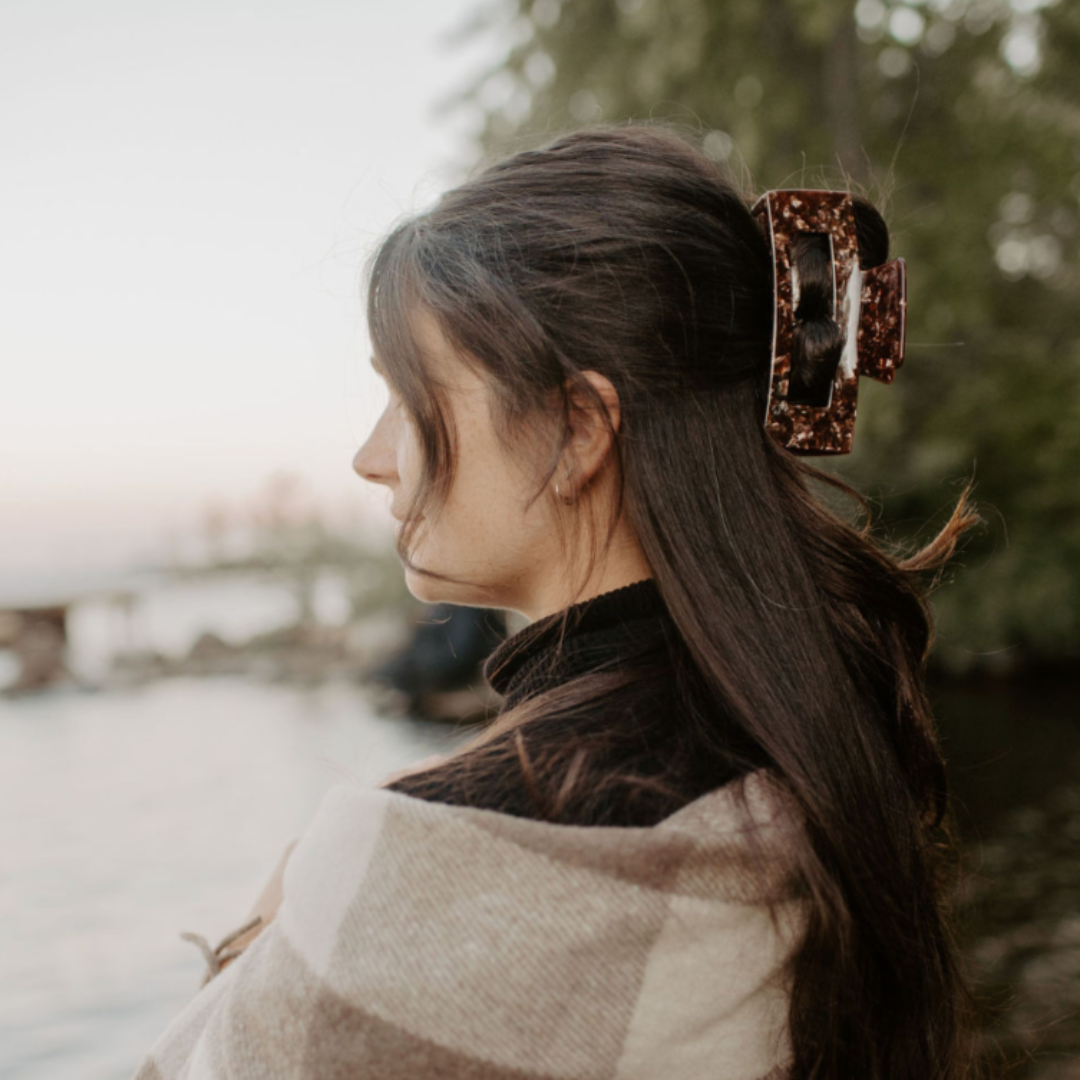 Woman with a striped shawl standing by a body of water with trees in the background