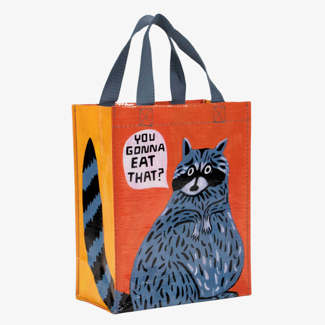 A reusable tote bag with a playful design. The bag is orange and yellow with a blue raccoon in the center. The raccoon is holding a piece of food and has a speech bubble above its head that says "YOU GONNA EAT THAT?" The bag has blue handles.
