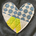 Heart-shaped patch with blue floral pattern and yellow center on a dark fabric background