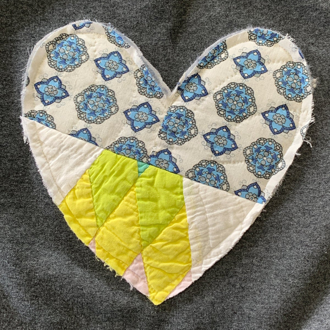 Heart-shaped patch with blue floral pattern and yellow center on a dark fabric background