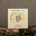 Eleven LoveManifest product packaging on a wooden surface with moss, against a brown background