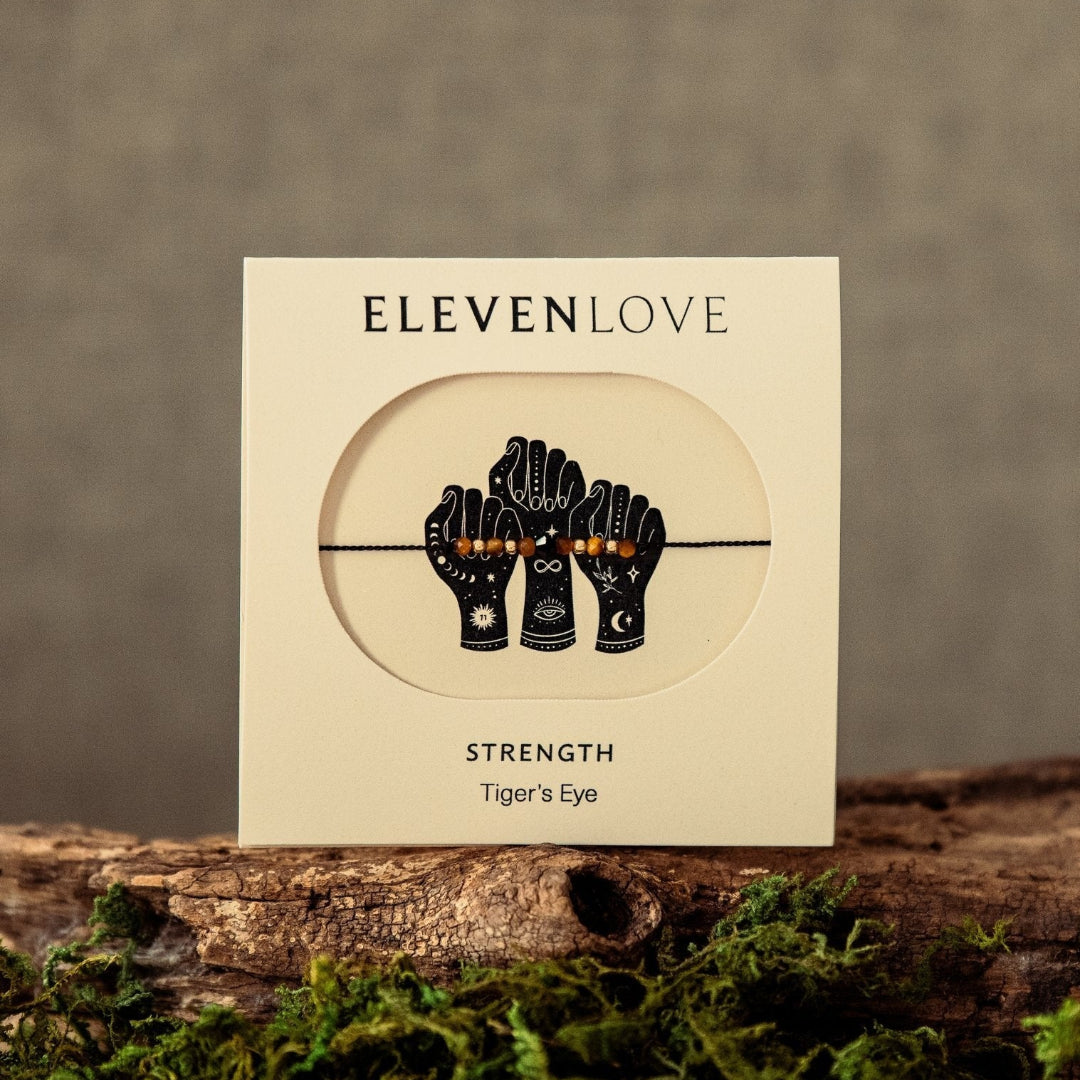 Card with 'Eleven Love' design featuring hands holding a string, on a wooden surface with moss.