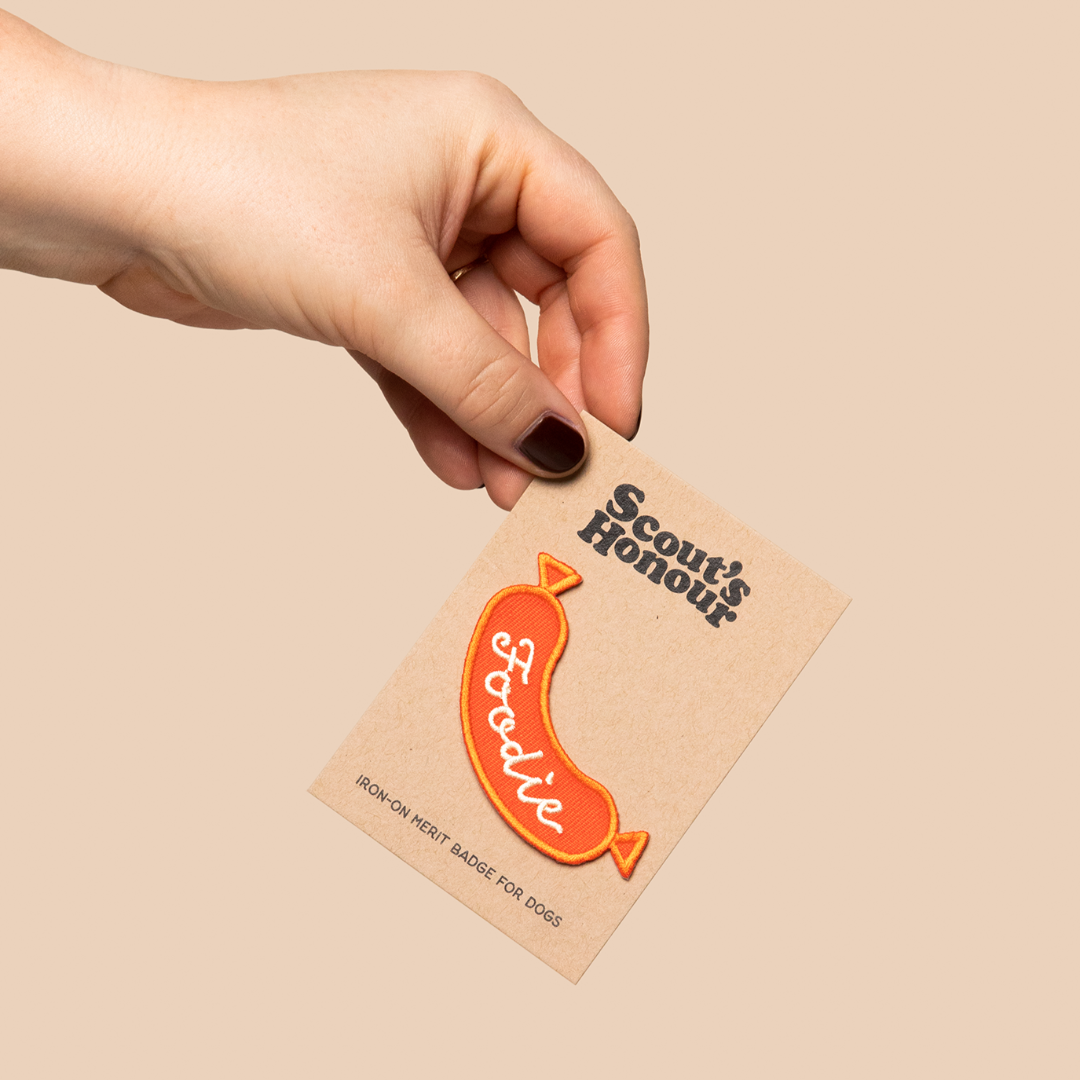 Hand holding a card with a foodie-themed badge on a beige background