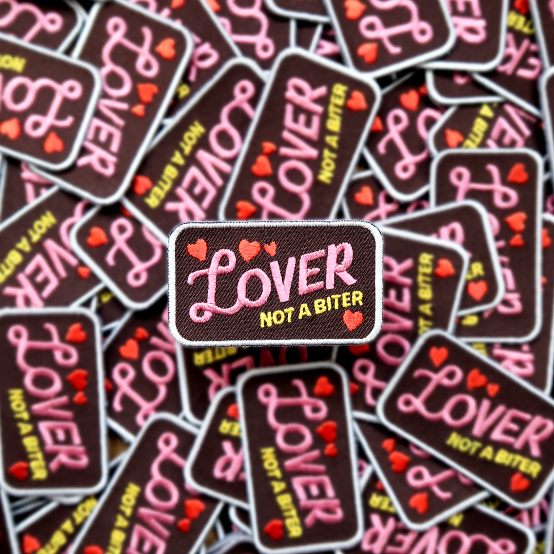 Collection of 'Lover Not a Biter' patches with pink and yellow text on a black background.