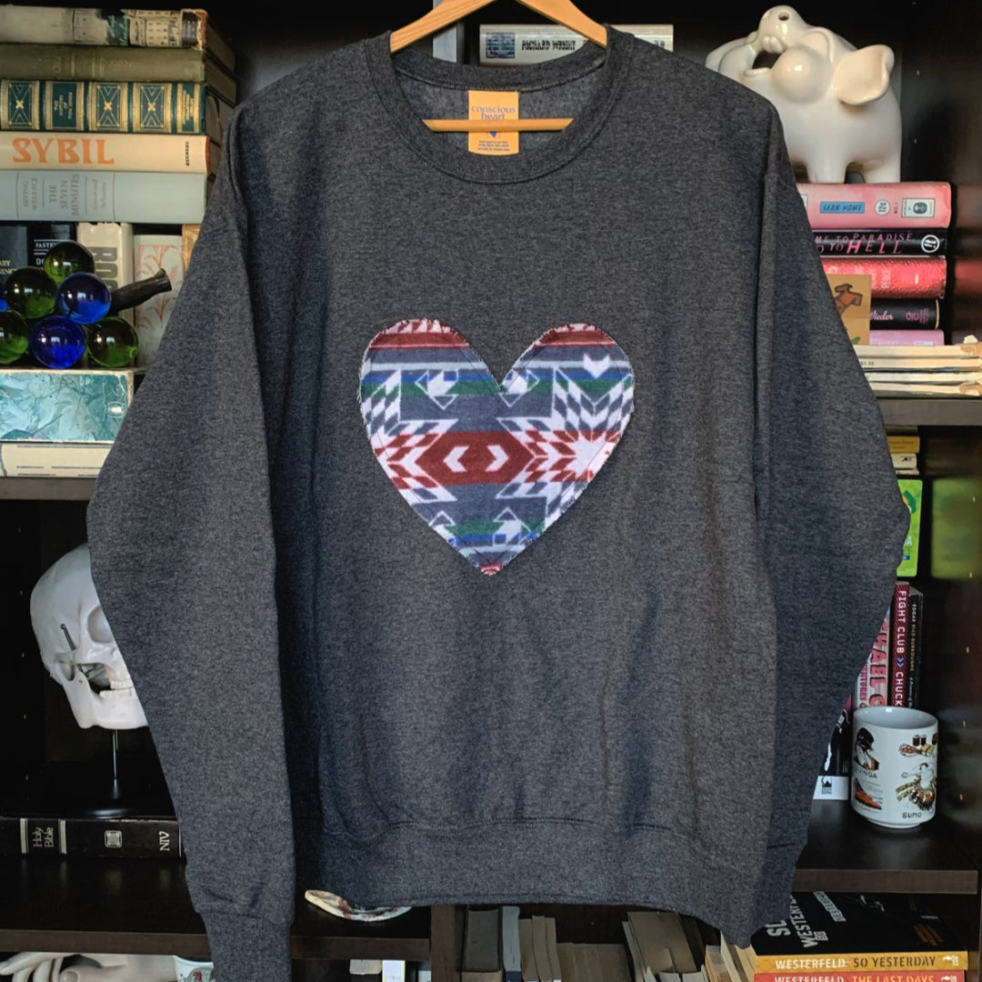 Gray sweatshirt with a colorful heart design on a hanger against a bookshelf background