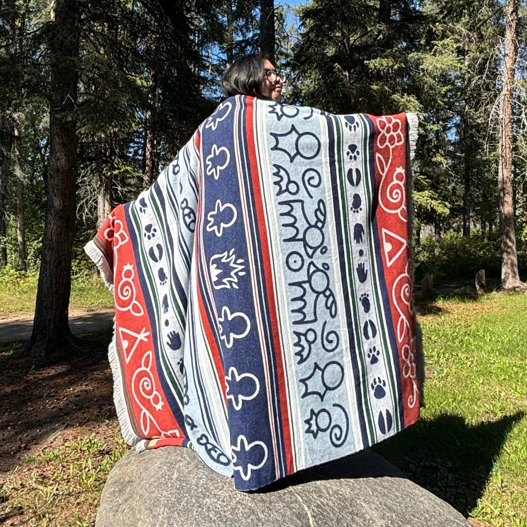 Person sitting on a rock outdoors with a colorful patterned blanket draped over them
