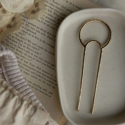 Brass crescent hair fork on ceramic dish with book underneath. 