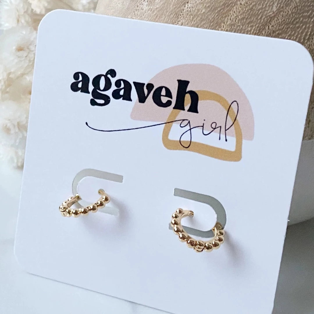 A pair of 14K Gold Ball Hoop Cuffs by agaveh girl, featuring a beaded design, displayed on a branded card with the text 'agaveh girl,' against a textured background. The earrings are dainty and high-quality, available in Ottawa, Ontario, Canada.