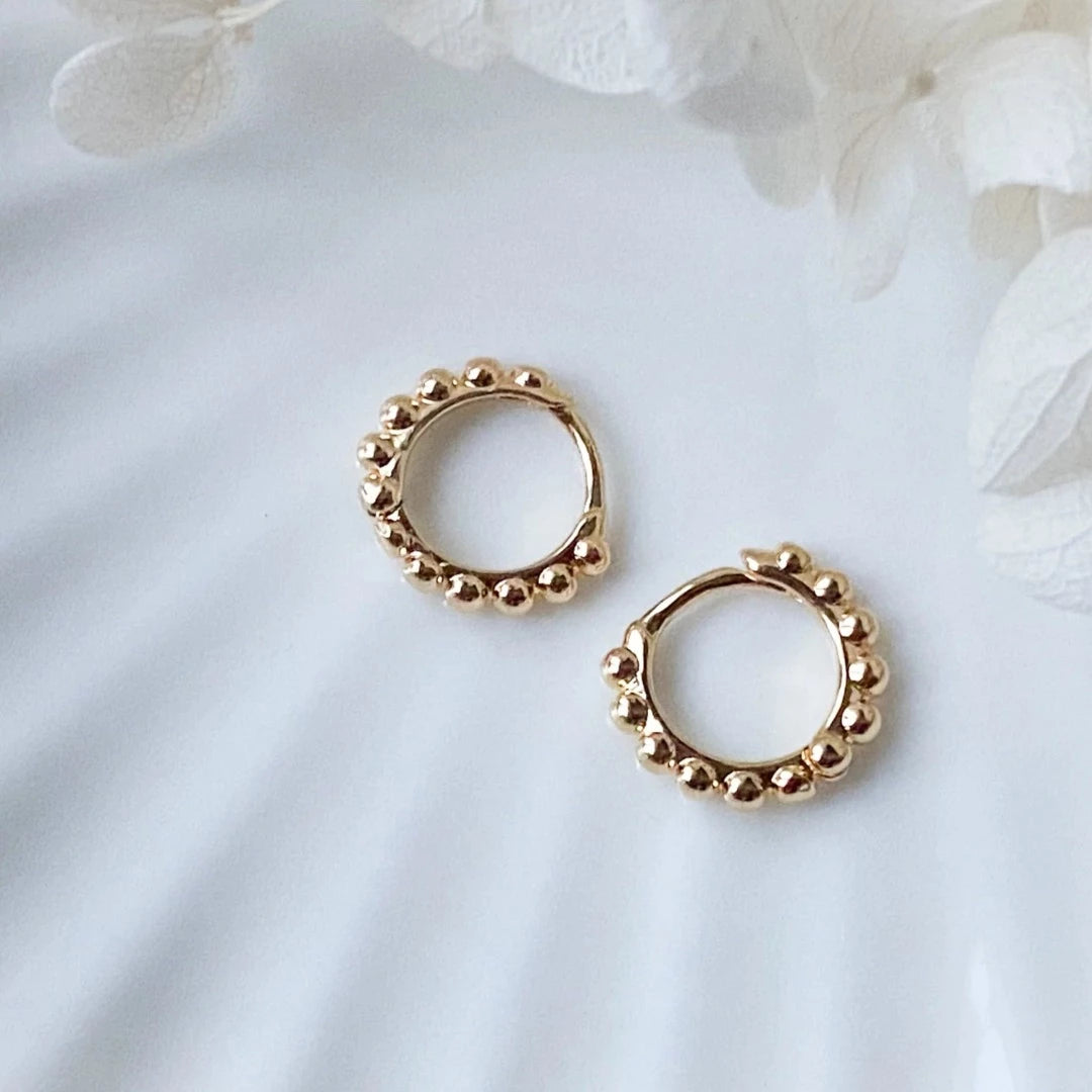 A pair of 14K Gold Ball Hoop Cuffs by agaveh girl, featuring a beaded design, displayed on a branded card with the text 'agaveh girl,' against a textured background. The earrings are dainty and high-quality, available in Ottawa, Ontario, Canada.