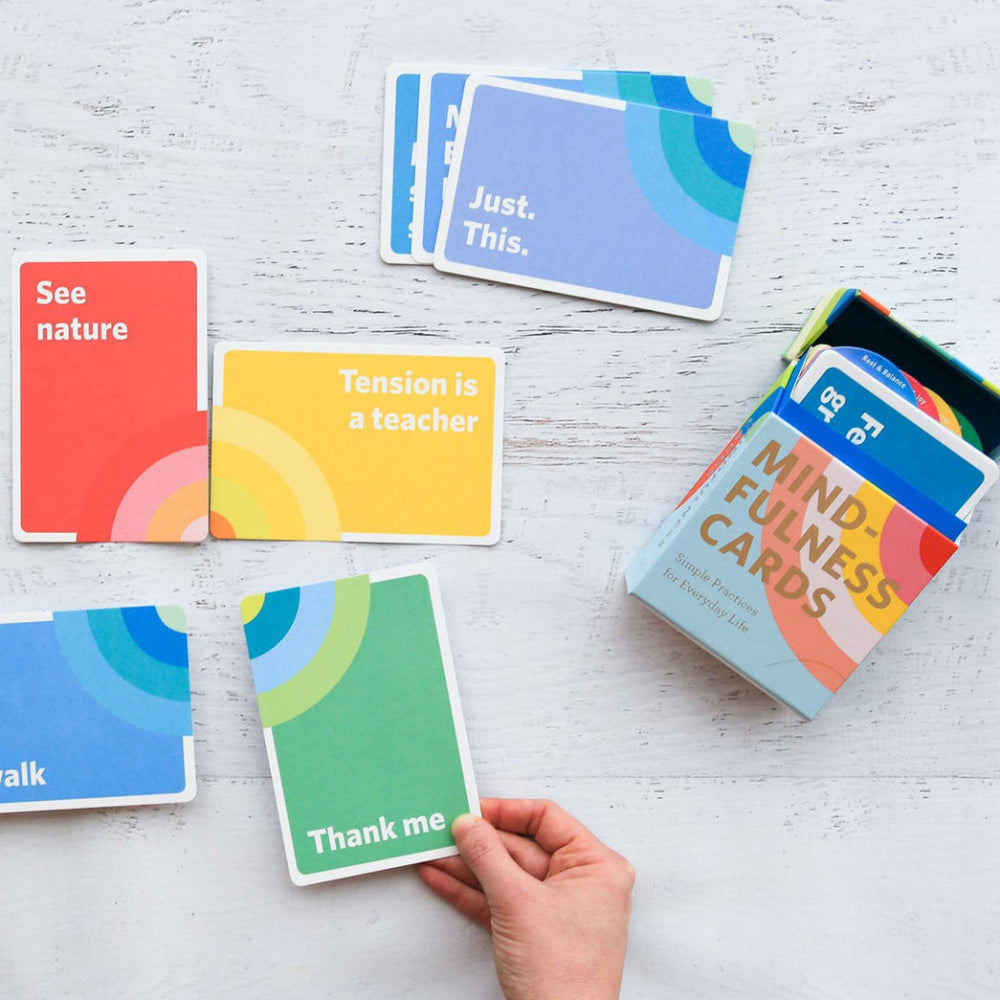 Card game box titled 'Poorly Explained TV Shows' on a yellow surface with cards around it.