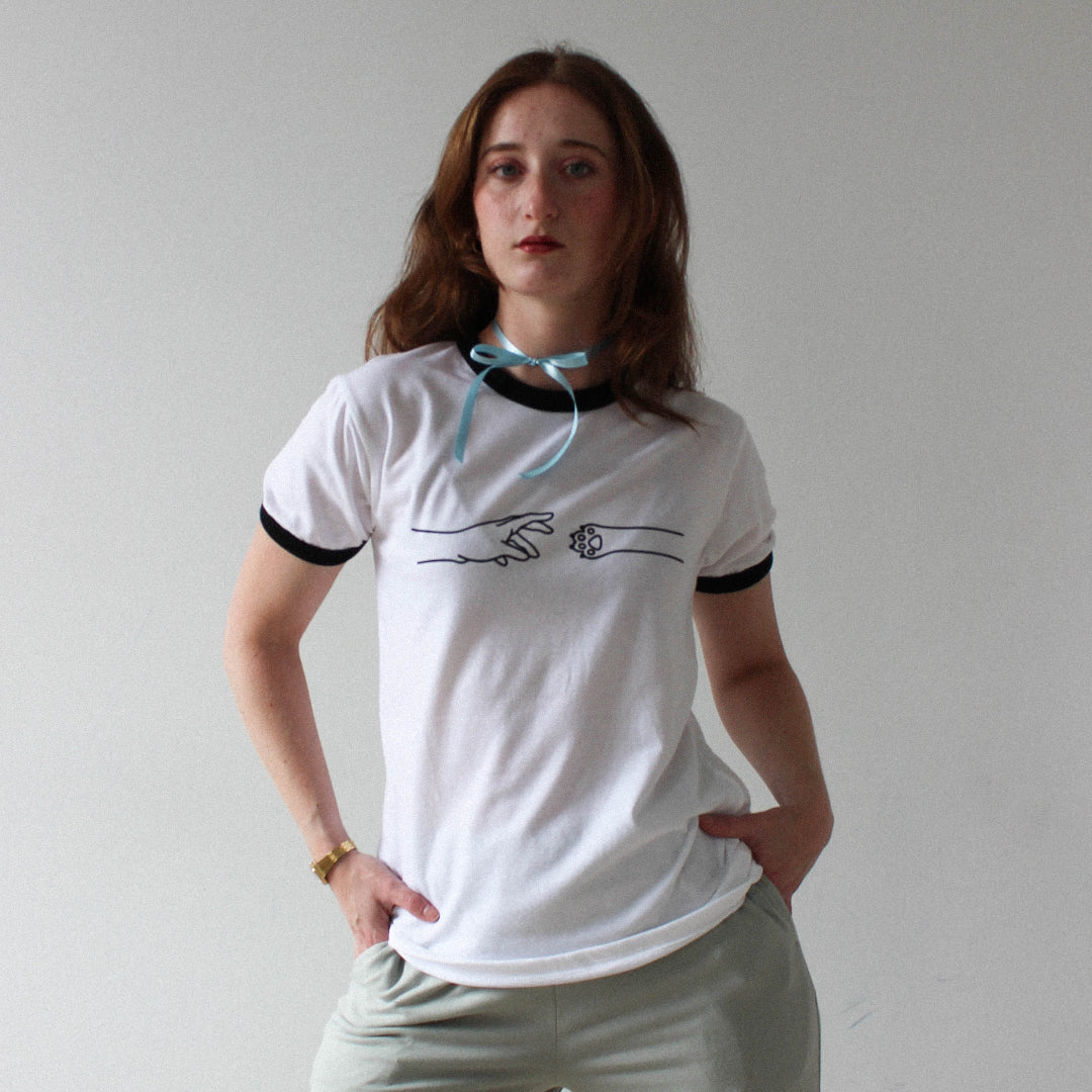 Person wearing a white t-shirt with black trim and light gray pants against a plain background