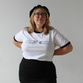 Person wearing a white t-shirt with black trim and a black skirt on a plain background