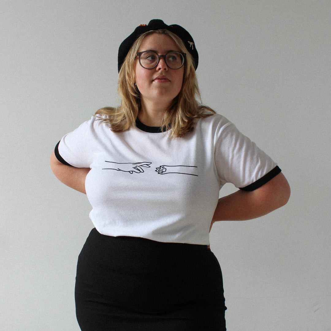 Person wearing a white t-shirt with black trim and a black skirt on a plain background