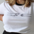 Person wearing a white t-shirt with black trim and a black skirt on a plain background