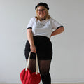 Person wearing a white t-shirt and black skirt, holding a red bag against a plain background