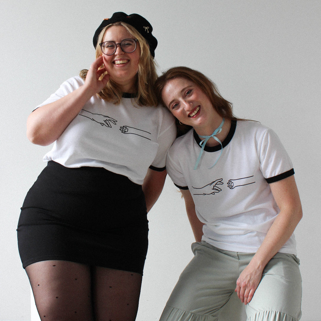 Two people wearing matching white t-shirts with black designs against a plain background