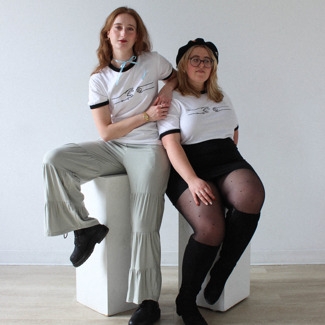Two people sitting on a white stool against a plain background