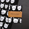 A black tea towel with a pattern of white cat faces. The cat faces are arranged in a grid-like pattern and vary in size and shape.