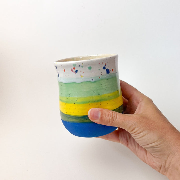 Peaceful Thumb Mug, a handless mug with a blue to green striped design and speckles finish.
