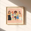 A framed art print featuring an illustration of five women in colorful outfits against a pink background, hanging on a beige wall with diagonal sunlight shadows.