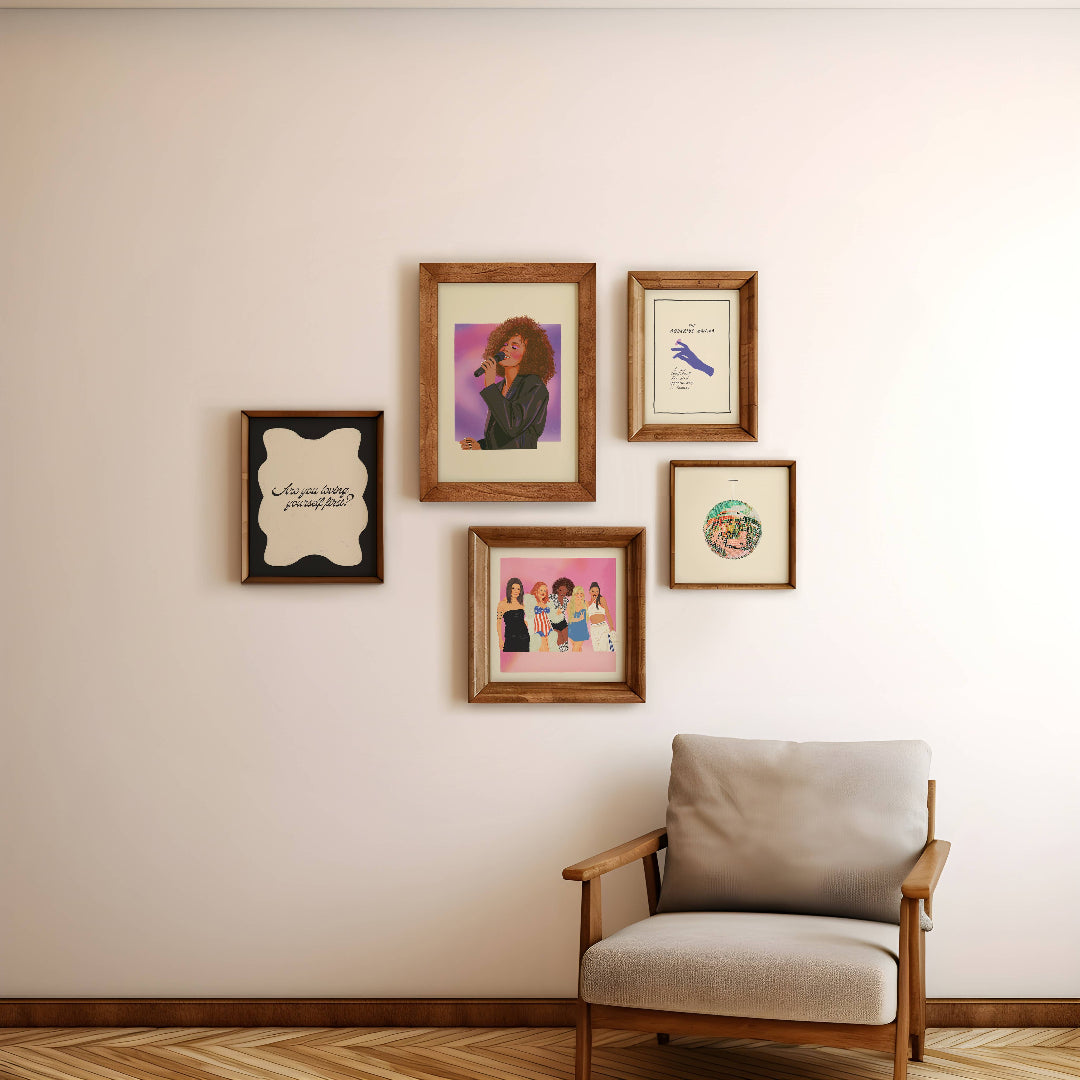 Five framed art prints in varying wood frames are arranged on a beige wall above a modern armchair with a light gray cushion and wooden frame.
