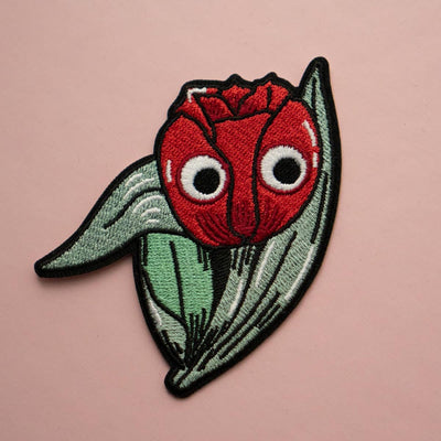 A red embroidered tulip with googly eyes and green leaves.