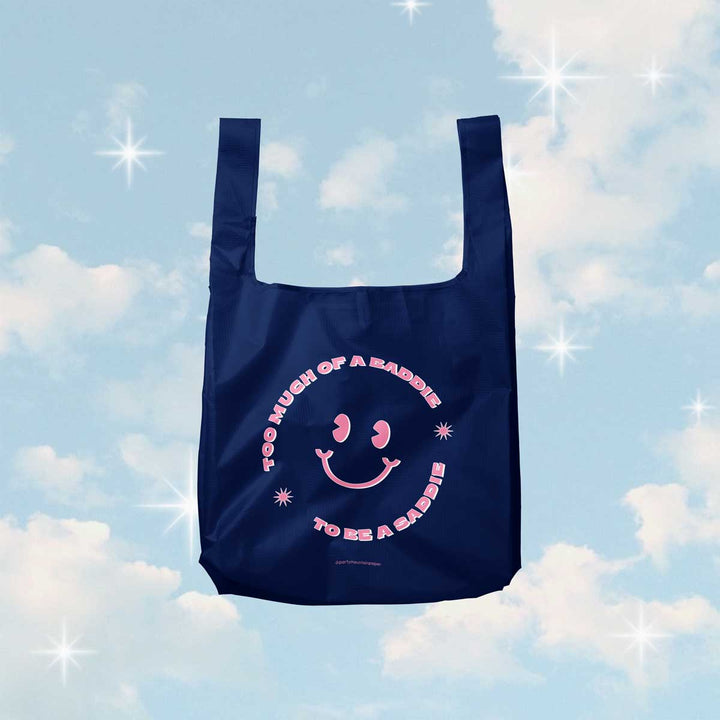 A navy blue, foldable tote bag with pink text and a smiley face. The text reads 