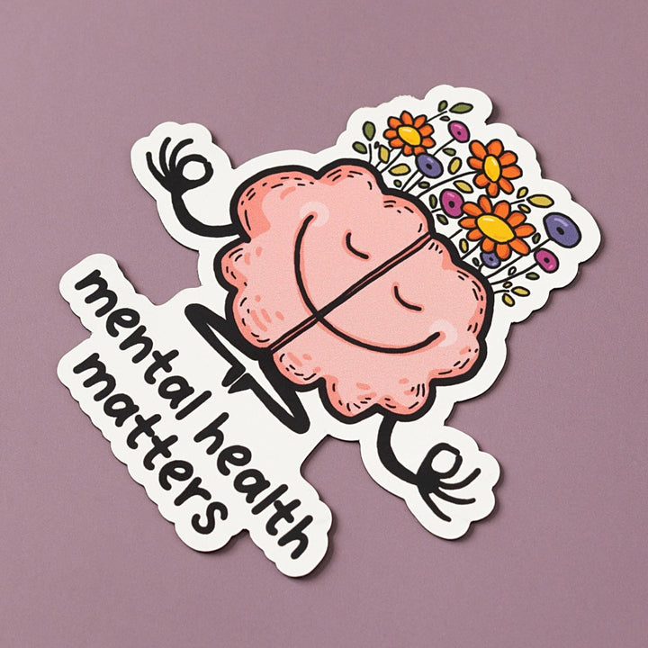 A pink cartoon brain with a smiling face is meditating. The brain has flowers growing from the top and is surrounded by the text 