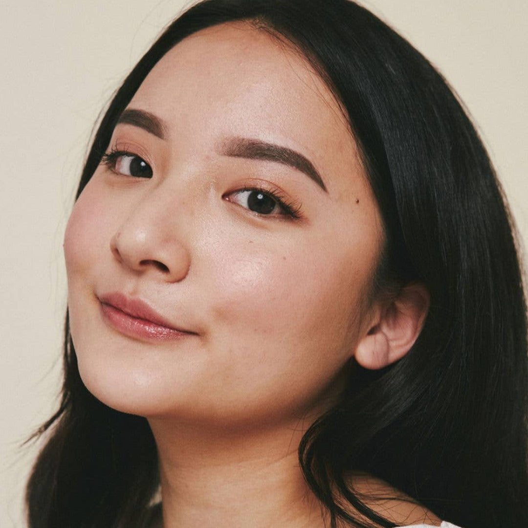 Sunset Glow Stick, a solid highlighter makeup stick in a warm coral pink sunset colour exampled on a women.