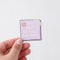 A hand holding a It's Okay To Have Bad Days Sticker, a white sticker with a purple post it reading 