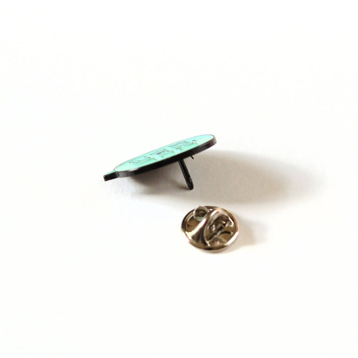 A mint green enamel pin in the shape of a speech bubble. The text 