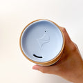 Mountains Travel Mug, a ceramic mug with a matte finish, with a mountain scape around the perimeter. Comes with a blue silicone lid.