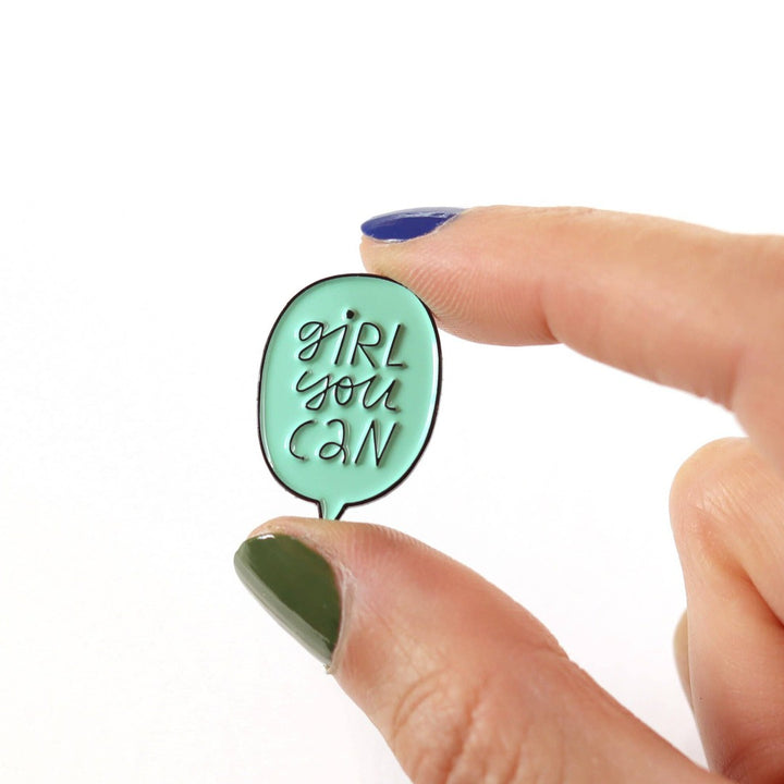 A mint green enamel pin in the shape of a speech bubble. The text 