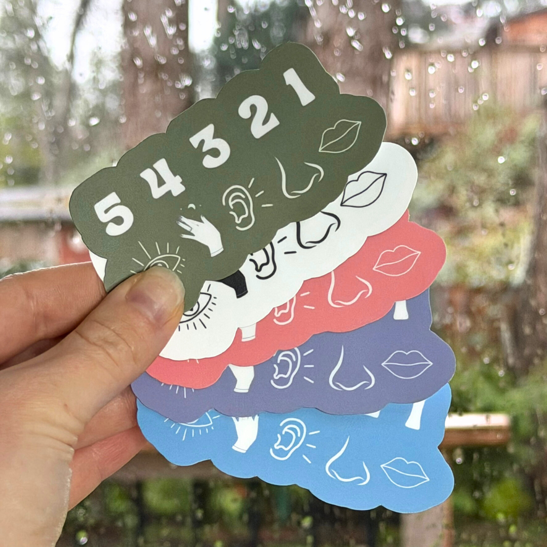 Stack of colorful stickers with various designs held by a hand outdoors.