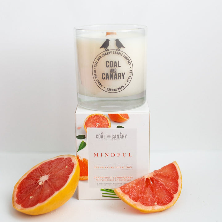 Mindful Candle, a glass jar candle with wood wick next to two slices of grapefruit