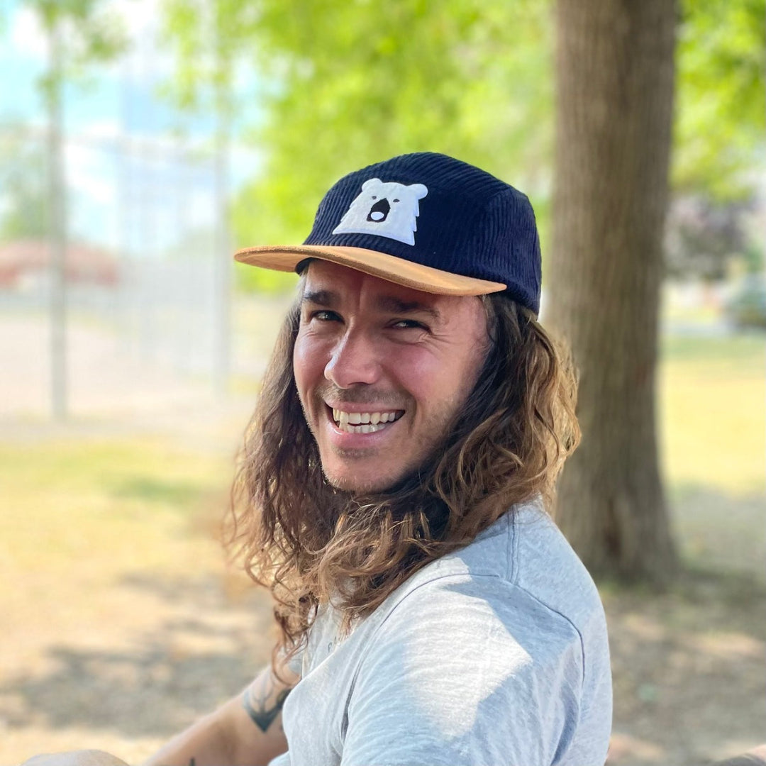 Man wearing a navy cap with a bear logo in a park setting