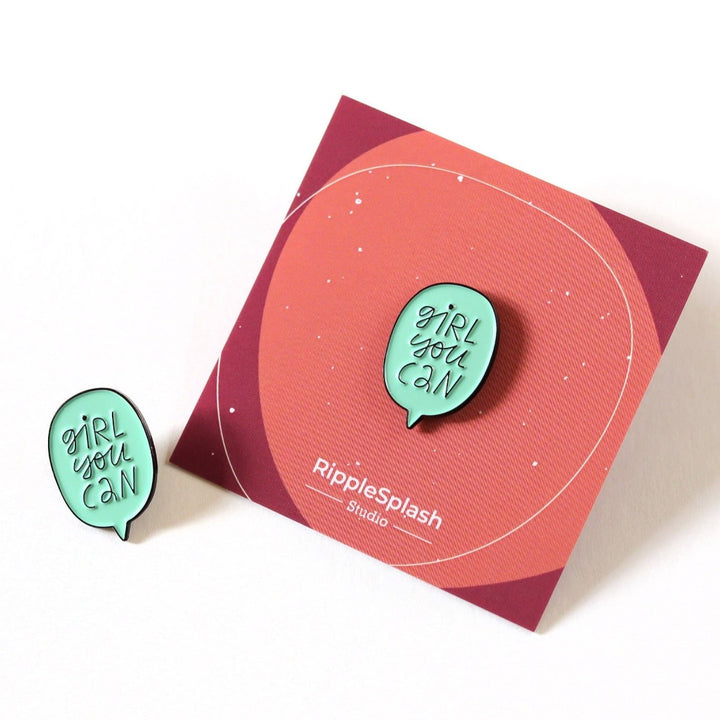 A mint green enamel pin in the shape of a speech bubble. The text 