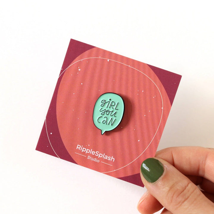 A mint green enamel pin in the shape of a speech bubble. The text 