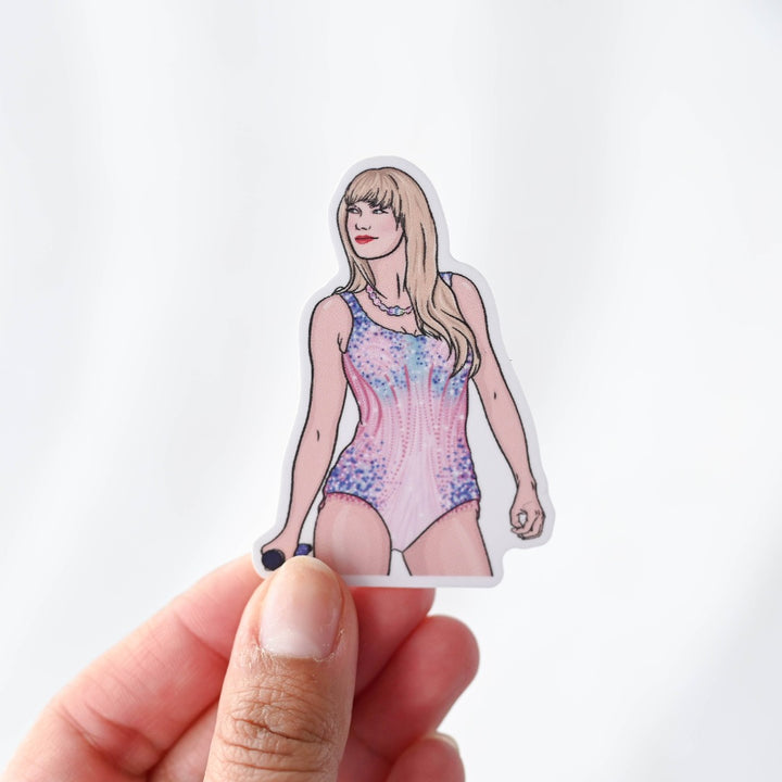 A hand holding a Taylor Lover Era Sticker, a white sticker with an image of Taylor Swift in her Lover bodysuit from the Eras Tour.