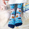 A pair of blue socks with a winter sports theme. The socks feature illustrations of skiers, snowboards, and a mountain cabin. The text 